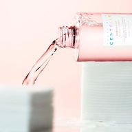 مایع شفافی از بطری با درپوش صورتی که روی آن برچسب "CENTELLA POREMIZING CLEAR TONER" قرار دارد، روی دسته پدهای پنبه‌ای سفید ریخته می‌شود.